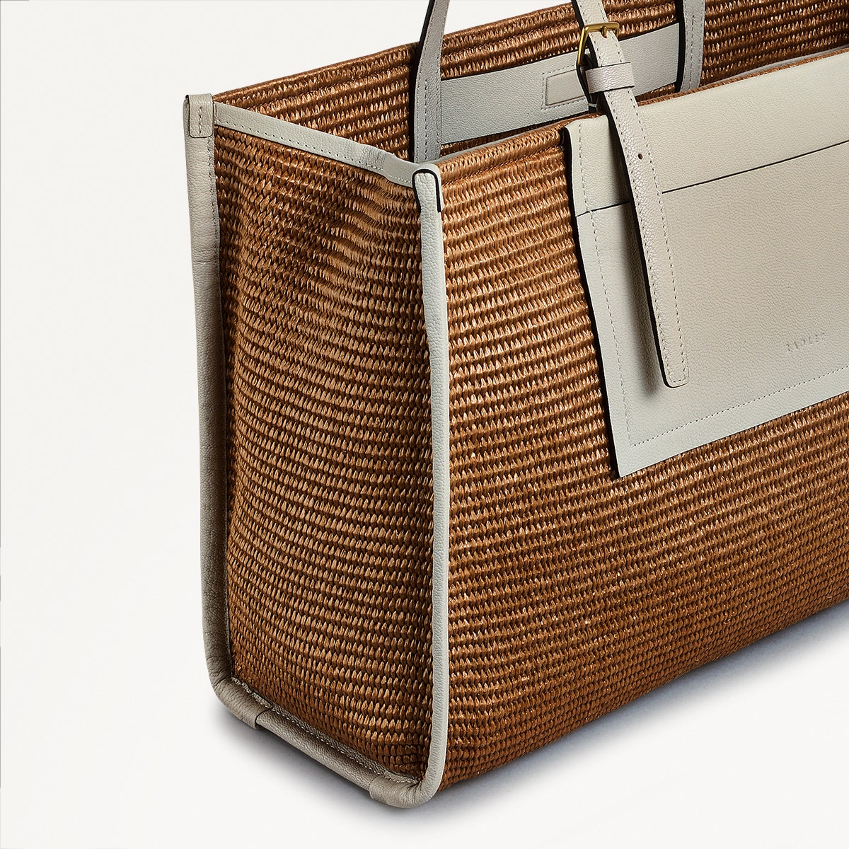 Brown woven handbag with beige leather handles on a light gray background