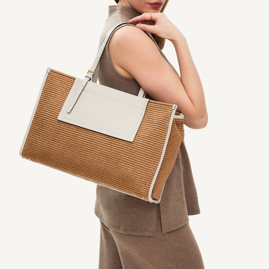Woman holding a brown and beige handbag against a neutral background