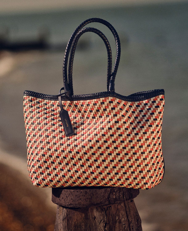 Woven handbag with a geometric pattern on a wooden post by a body of water.