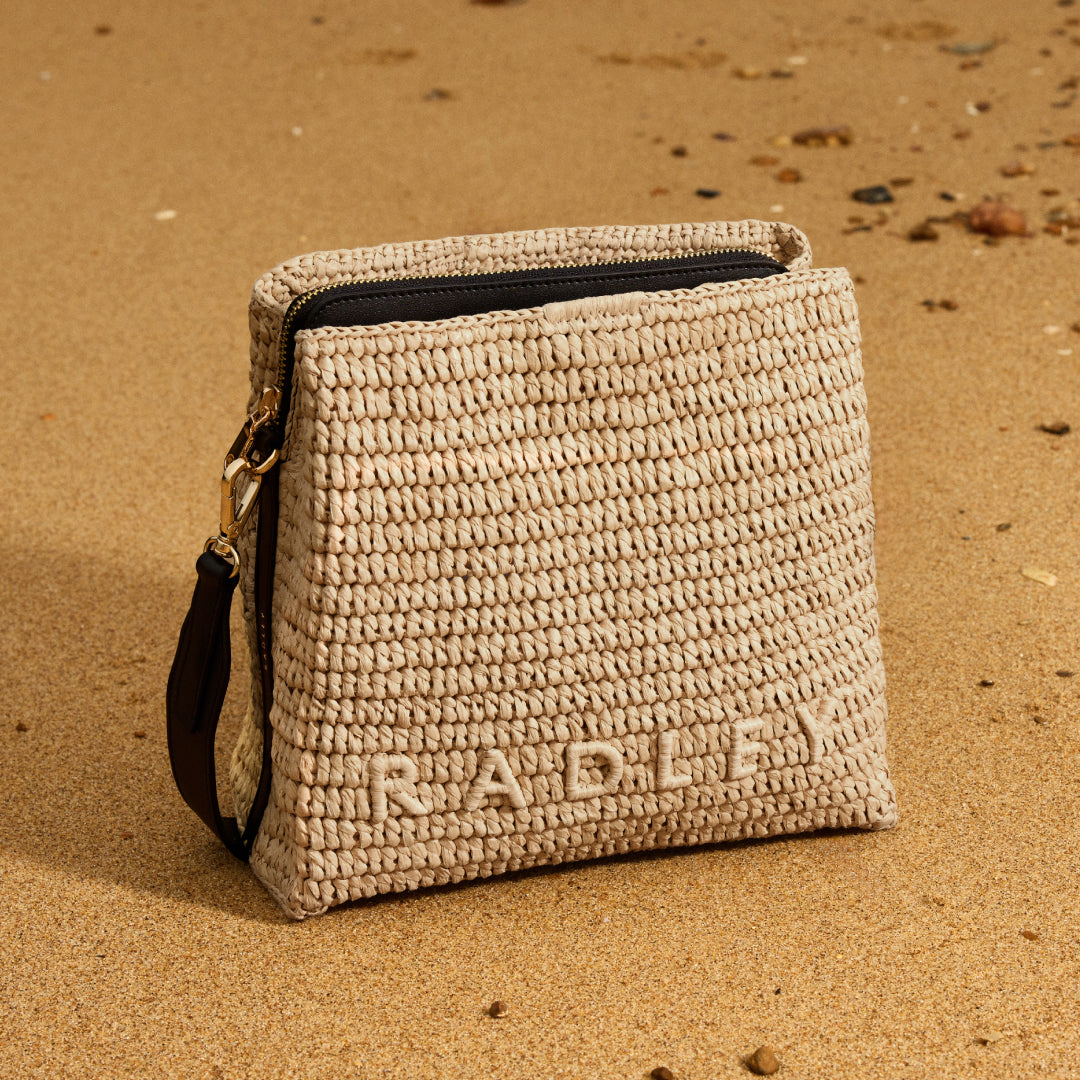 Beige woven pouch with 'RADLEY' branding on a sandy background