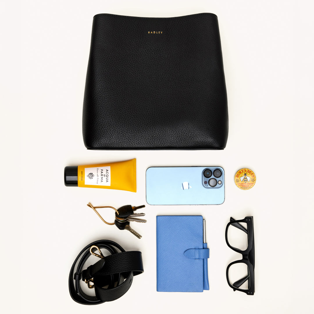 Black leather bag with various items including a phone, keys, and a notebook on a white background