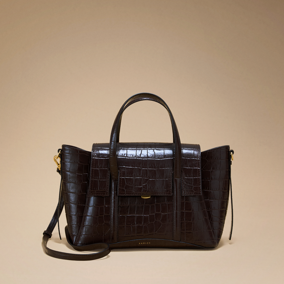 Brown leather handbag with crocodile texture on a beige background