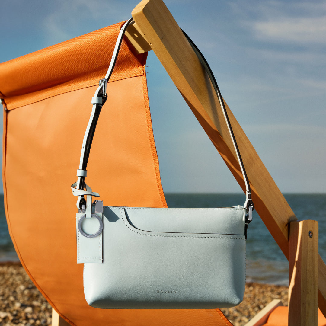 Light blue handbag hanging on an orange beach chair with a sea view in the background