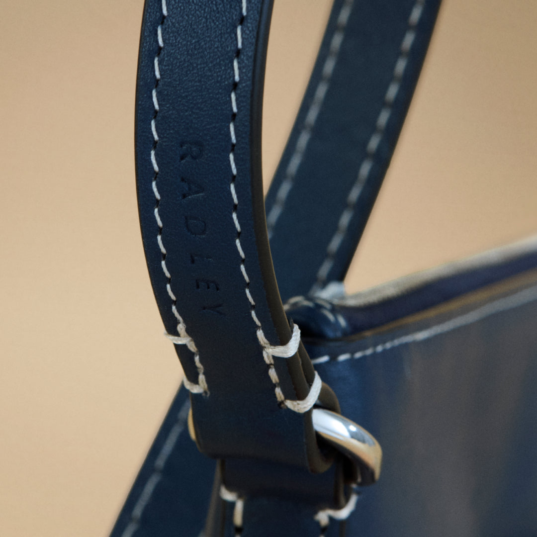 Close-up of a navy blue leather strap with white stitching on a beige background