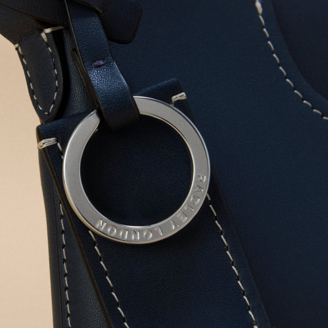 Close-up of a navy blue leather strap with a silver ring and visible brand name.
