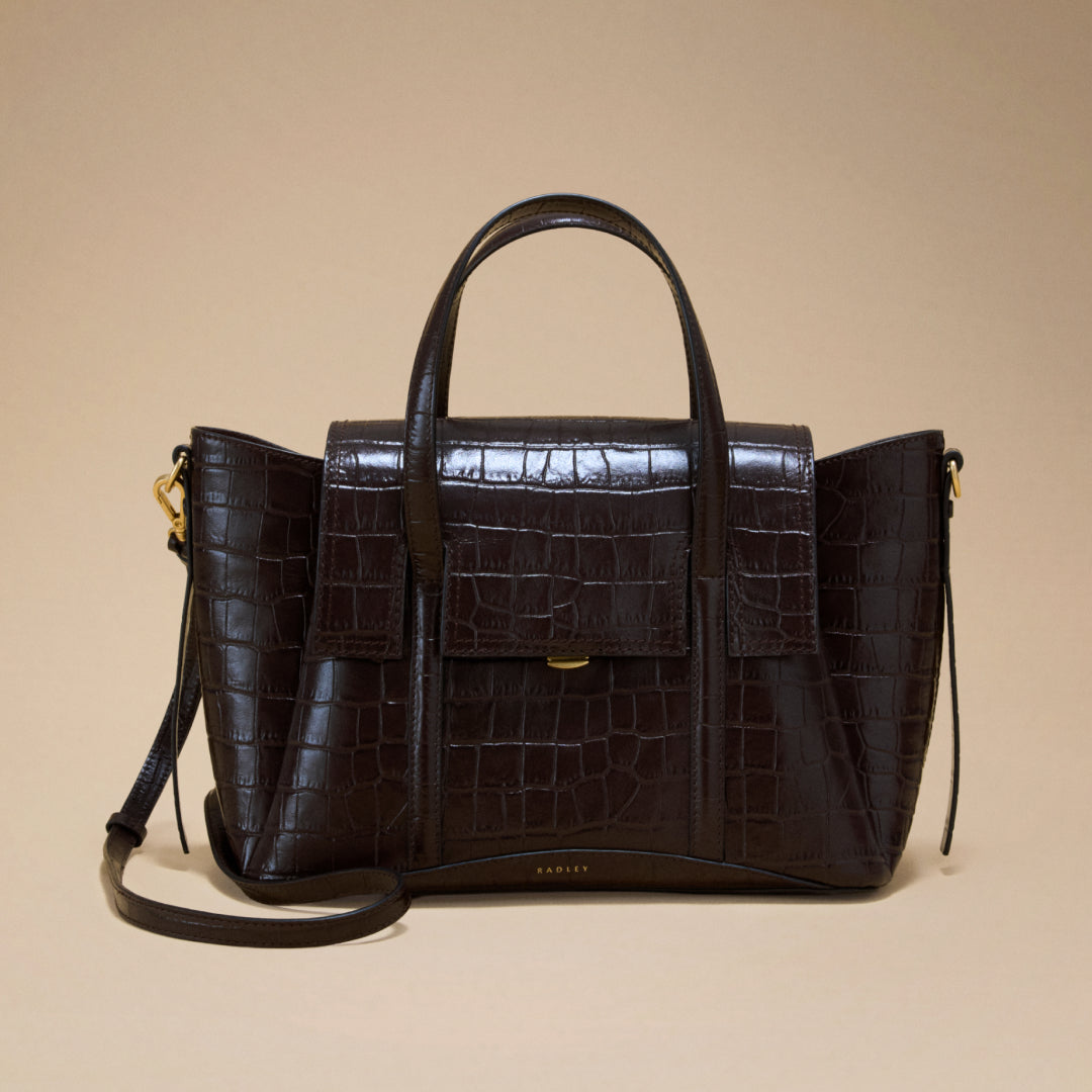 Brown leather handbag with crocodile texture on a beige background