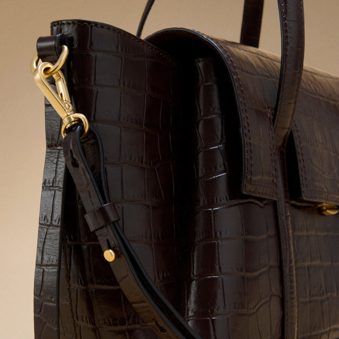 Brown textured leather handbag with gold hardware on a beige background