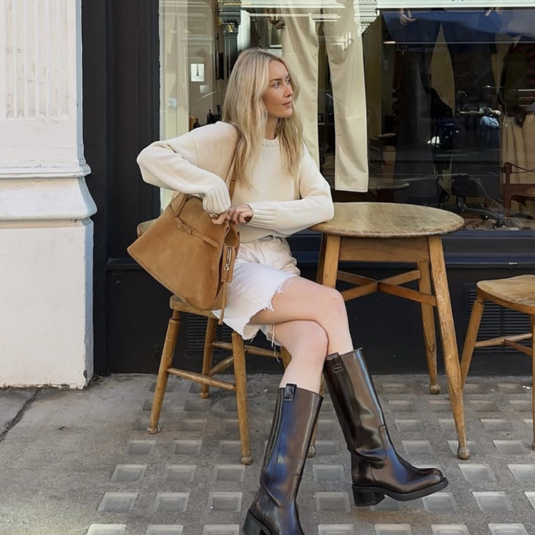 Woman sitting on a chair outside a cafe holding a brown bag.