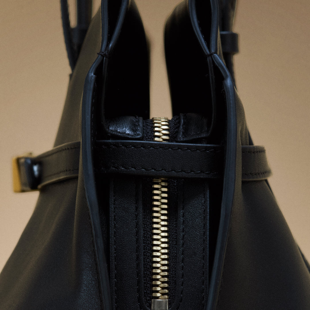 Close-up of a black leather bag with a gold zipper on a beige background