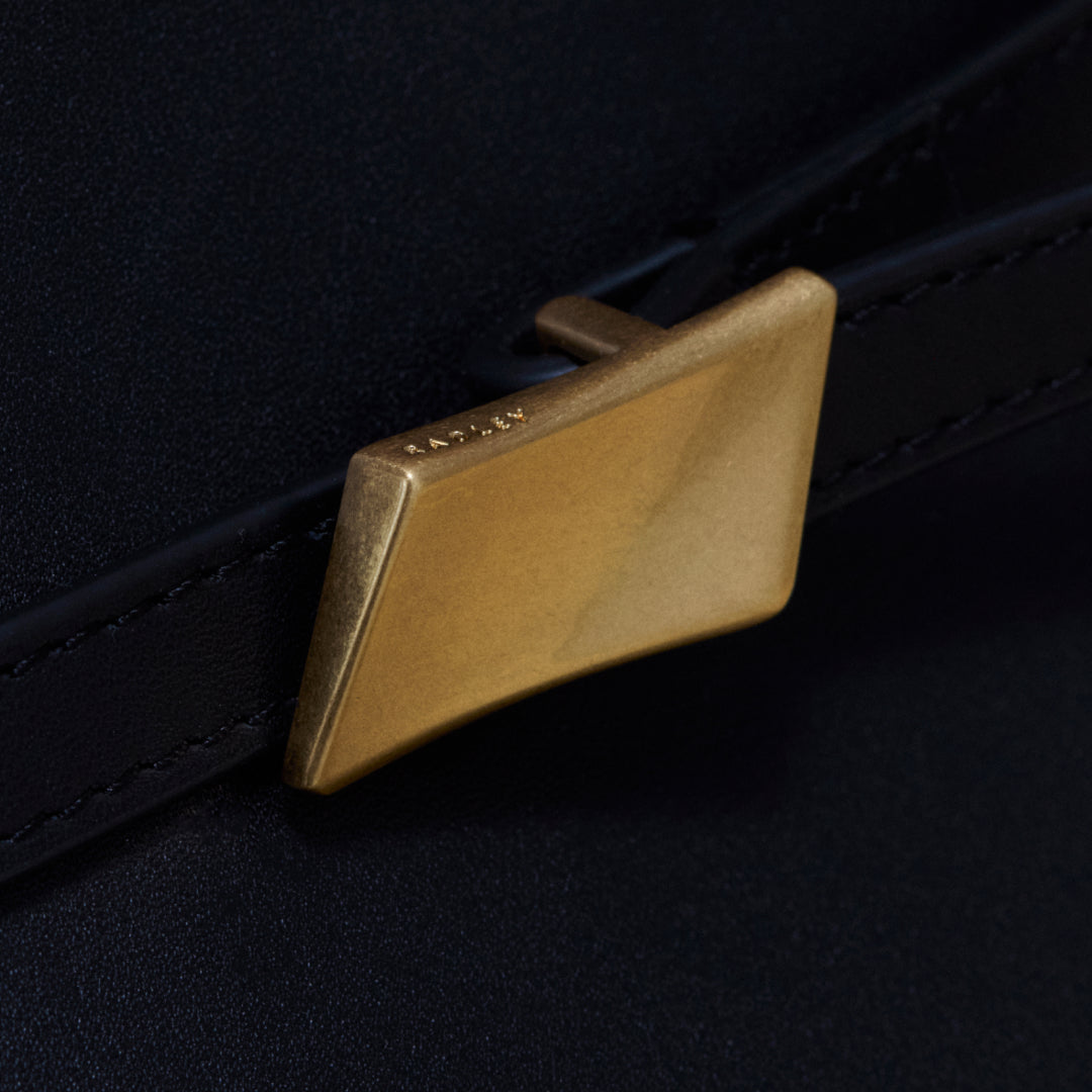 Brass belt buckle on a black leather belt against a dark background