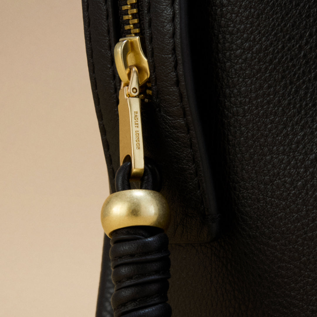 Close-up of a black leather bag with a gold zipper pull on a beige background