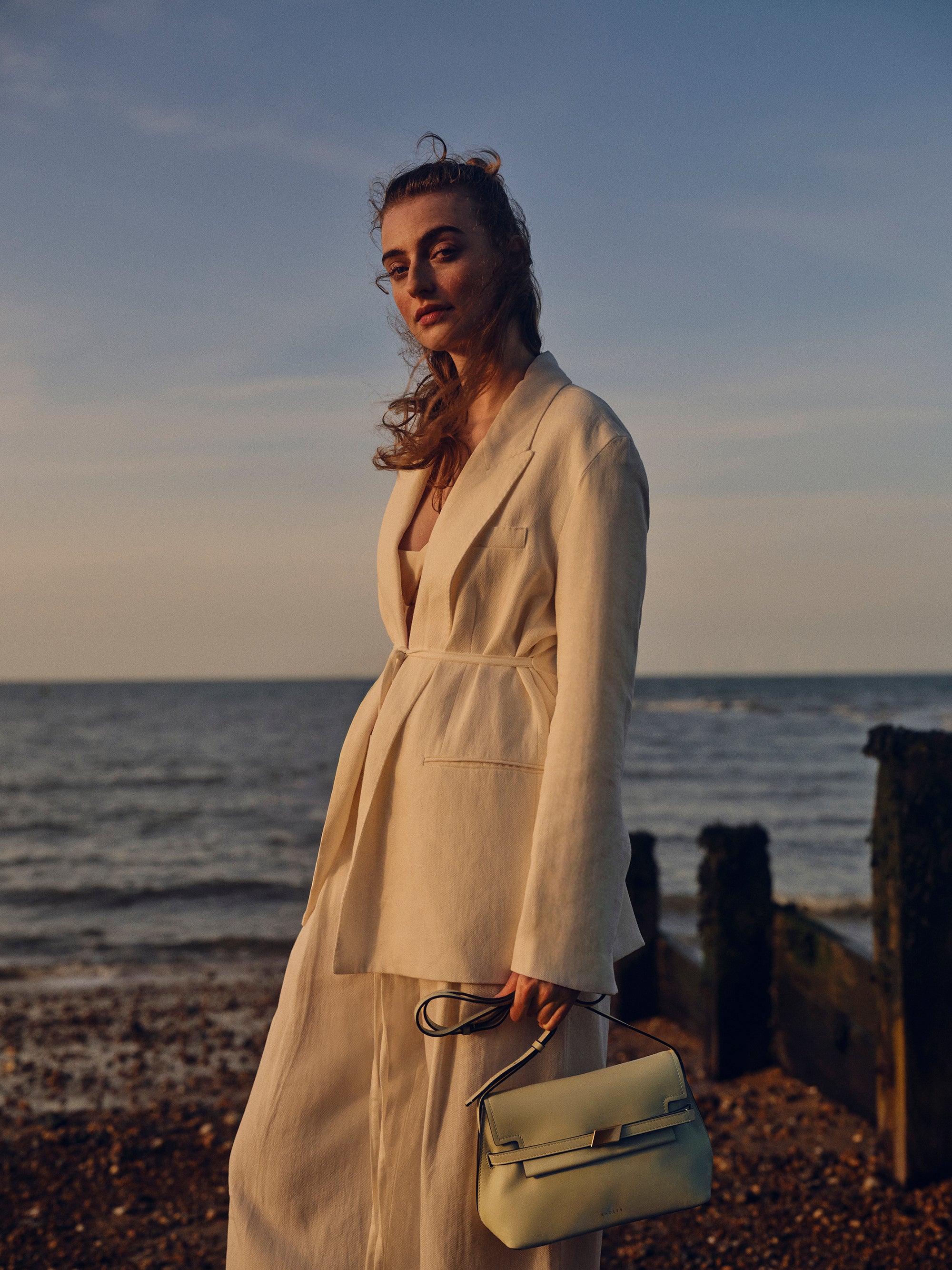 Woman in a beige outfit standing on a beach with ocean and sky in the background